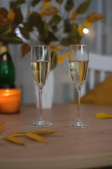 autumn home decoration. Two glasses of champang, vase autumn yellow leafes,candle on round wooden table.