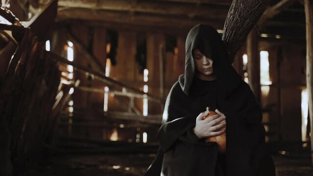 A teenage girl is dressed in old rags, sitting in a shed surrounded by the main symbol of Halloween. She is holding a pumpkin, as soon as the camera approaches her, she will look up and look at you.