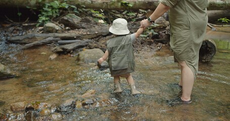 happy family mother holding hand cute little Asian toddler daughter walking in mountain river water creek Learning about Nature in the rainforest, adventure explorer camping travel trip