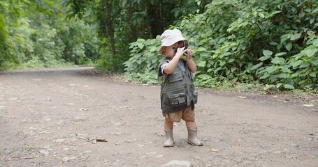 Fototapeta premium Happy Tourist cute little Asian toddler daughter kid girl using binoculars watching animals in the forest natural background, adventure explorer camping travel trip Learning about Nature