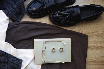 White shirt, knit cardigan, gray trousers, loafers, book, reading glasses and rings on wood...