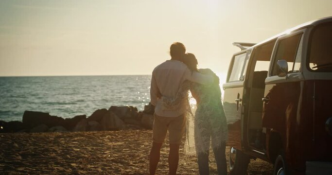 Backview Slow Motion Shot of a Couple Having a Romantic Getaway by the Beach Using their Minivan. Newlywed Couple Enjoying Their Honeymoon on a Beautiful Island, Hugging During Sunset