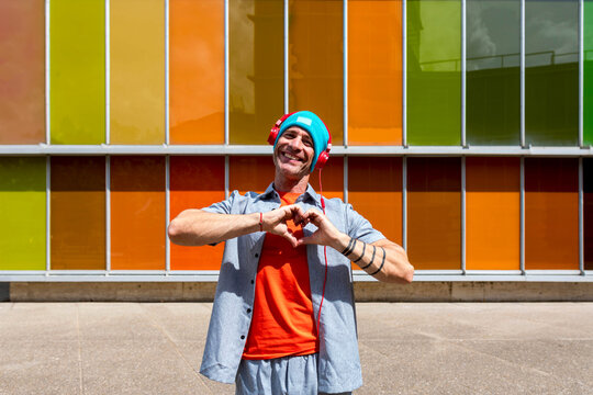 Man making heart gesture with hands near colorful building