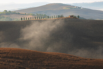 Morning mist through the valley of Val d'Orcia in the scenic countryside farmland and rolling hills of rural Tuscany, Italy.