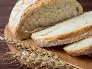 Close-up of fresh crispy wheat bread sliced lies on a wooden board. Wooden brown background. several ears of wheat are lying next to the bread. Side view