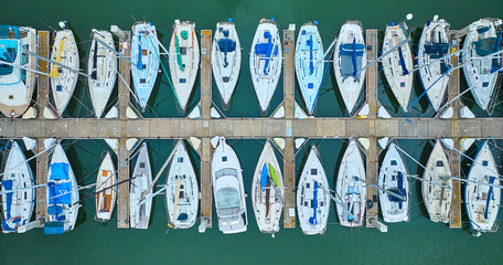 Aerial straight down close up view row of boats on pier dock area with teal ocean water
