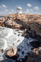 Rocky coastline. The waves break on the rocks. Beautiful landscape. The sky is the sea and the horizon. The old rotunda.