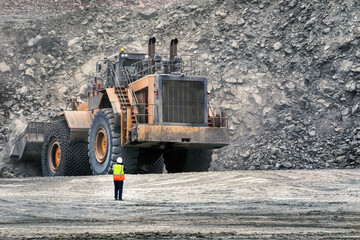 open pit diamond mine worker next to giant wheel loader moving machine, loading kimberlite
