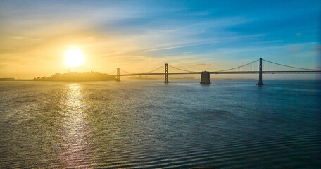 Aerial gold and blue sunrise over San Francisco Bay with sun coming over island and Oakland bridge