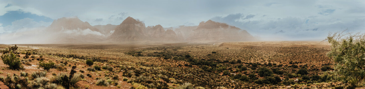 Panoramic landscape photography made from several photos of Redrock National Park in the State of Nevada, United States. You can see the desert valley and the enormous red rock mountains.
