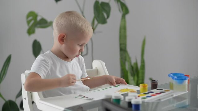 happy child draws with brush and paints on paper, boy spends time at home painting