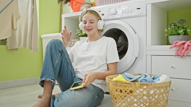 Young blonde woman listening to music dancing at laundry room