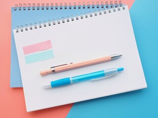 Blank notebook and pens on a pink and blue background 