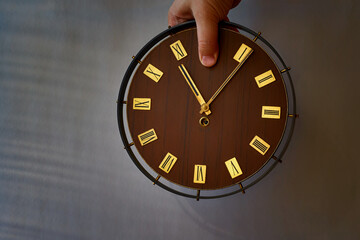 Old clock with Roman numerals on the dial and a person's hand covering the number 12. Passage of time, stop time, clock adjustment