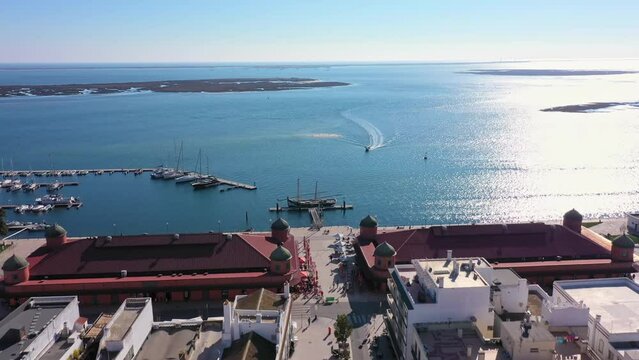 Aerial drone footage of the Portuguese southern town of Olhao. View of the municipal market and the sea in the background with a boat.