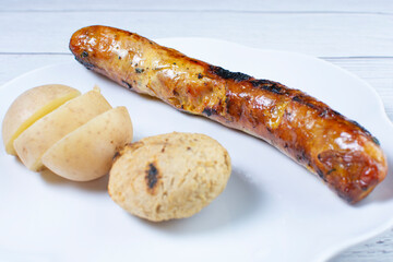 fried chorizo, potato flared and arepa on a white plate and light wooden background
