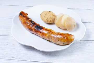 fried chorizo, potato flared and arepa on a white plate and light wooden background