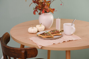 Home autumn breakfast, two toasts with almond butter, figs, coffee, pumpkins, candle, ceramic vase with red leaves on a round wooden table