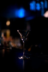 Clear and transparent cocktail glass standing on bar counter on blurred background
