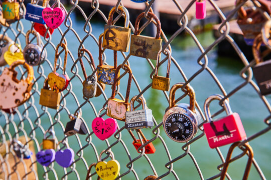 Variety of love and heart shaped locks on chain link fence with water in background