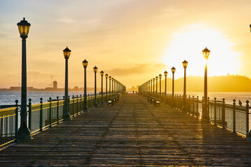 Sunrise over Pier 7 lined with benches and street lights on San Francisco Bay_