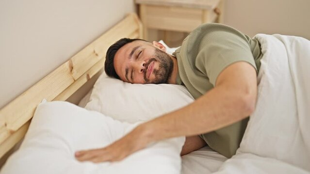 Young hispanic man covering ears for noise lying on bed at bedroom