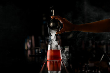 Hand of girl bartender accurate pours steaming cocktail from steel shaker into drinking glass with...
