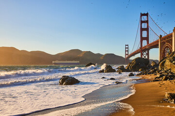 Crashing wave near sandy beach with seagulls above Golden Gate Bridge
