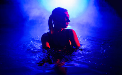 Sensual woman in leather BDSM mask dancing in swimming pool, neon light. - obrazy, fototapety, plakaty