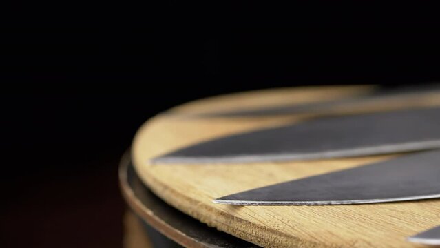Close up, Set of Knives Rotate on a Wooden Turntable on a Black Background. Sharp blades of steel kitchen knives. Professional knives for the chef. Cutlery. Wooden background, blur. Cooking concept.