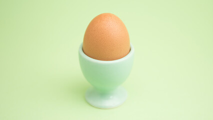  A single brown egg in a light green egg cup against a pale green background, showcasing a minimalist and calming aesthetic.