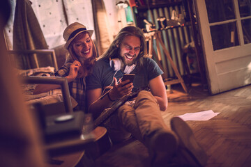 Happy young couple laughing with a smartphone on the bedroom floor at home - obrazy, fototapety, plakaty