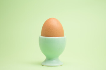  A single brown egg in a light green egg cup against a pale green background, showcasing a minimalist and calming aesthetic.