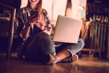 Close up of young woman sitting on the floor and using a smartphone with laptop