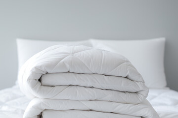 Fototapeta na wymiar White several folded duvets lying on white bed background. Preparing for winter season, hotel or home textile