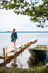 Fototapeta premium A woman in a dress in sunset light walks along a wooden bridge on the shore of the lake