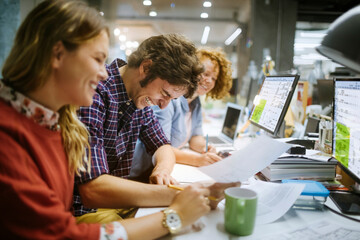 Diverse group of people laughing at paperwork in a modern office