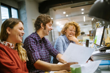 Diverse group of people laughing at paperwork in a modern office