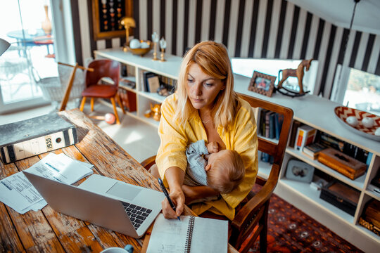 Loving mother breastfeeding her child and going through bills at home