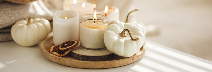 Autumn home decor with white pumpkins and burning aroma candles with sweet spicy pumpkin pie scent. Cozy fall composition, relaxation, aromatherapy. Apartment design, living room or bedroom banner