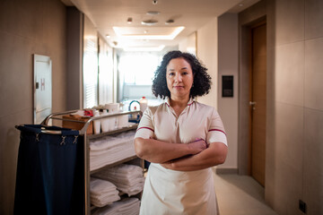 Portrait of a confident young cleaning lady posing in the hotel hallway