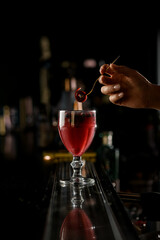 close-up on cocktail glass with brown liquid and woman's hand holding small fork with Pastille above it