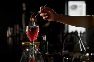 View on cocktail glass with red liquid and woman's hand holding small fork with Pastille above it