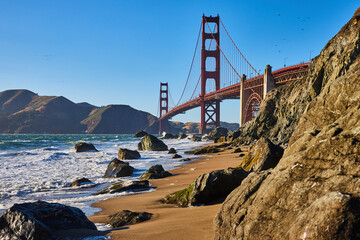 Boulder strewn terrain on sandy shore with waves and Golden Gate Bridge