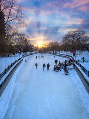 Colourful sunset sky over Patterson Creek during winter, people skating on frozen Rideau Canal, Glebe, Ottawa, Ontario, Canada. Photo taken in January 2021.