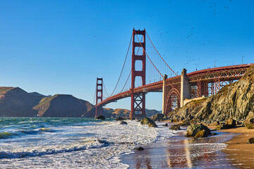 Waves crashing against sandy beach with boulders with Golden Gate Bridge in background