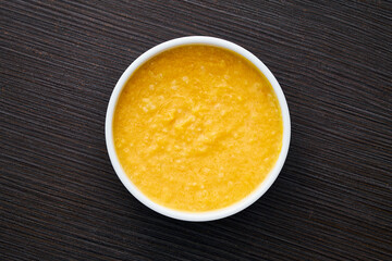 A bowl of pumpkin porridge on a textured dark brown table - an appetizing blend of Thanksgiving and healthy dining, embodying the essence of nourishing traditions. Top view.