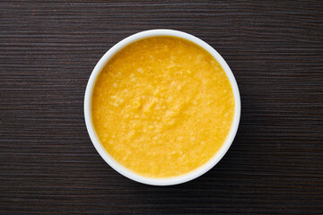 A bowl of pumpkin porridge on a textured dark brown table - an appetizing blend of Thanksgiving and healthy dining, embodying the essence of nourishing traditions. Top view.