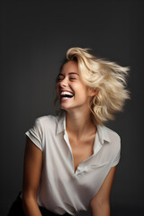 A beautiful young blonde girl, wearing a white shirt, looking to the left and laughing with her hair in the wind with a dark grayish background, top light
