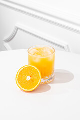 Orange juice in a glass on a white table, sunny hard light.